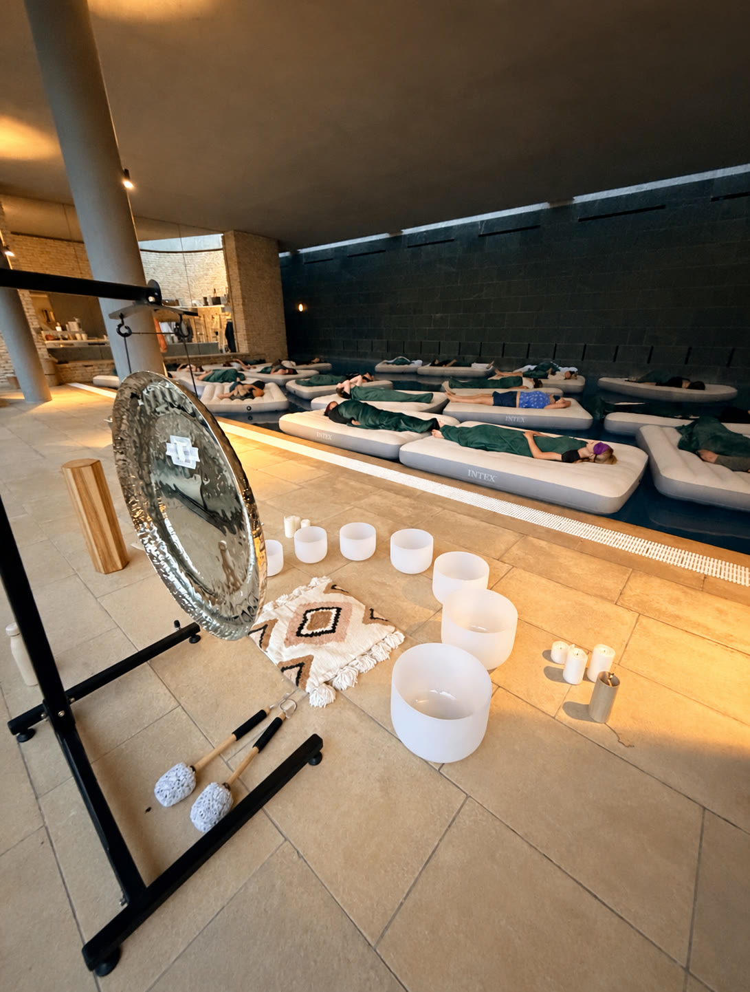 Guests relaxing on floating beds at Cowley Manor with a gong and crystal singing bowls beside the pool