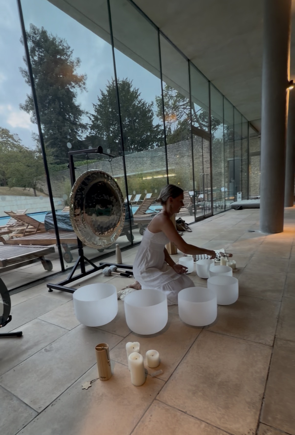 A sound practitioner playing crystal singing bowls beside the pool at Cowley Manor