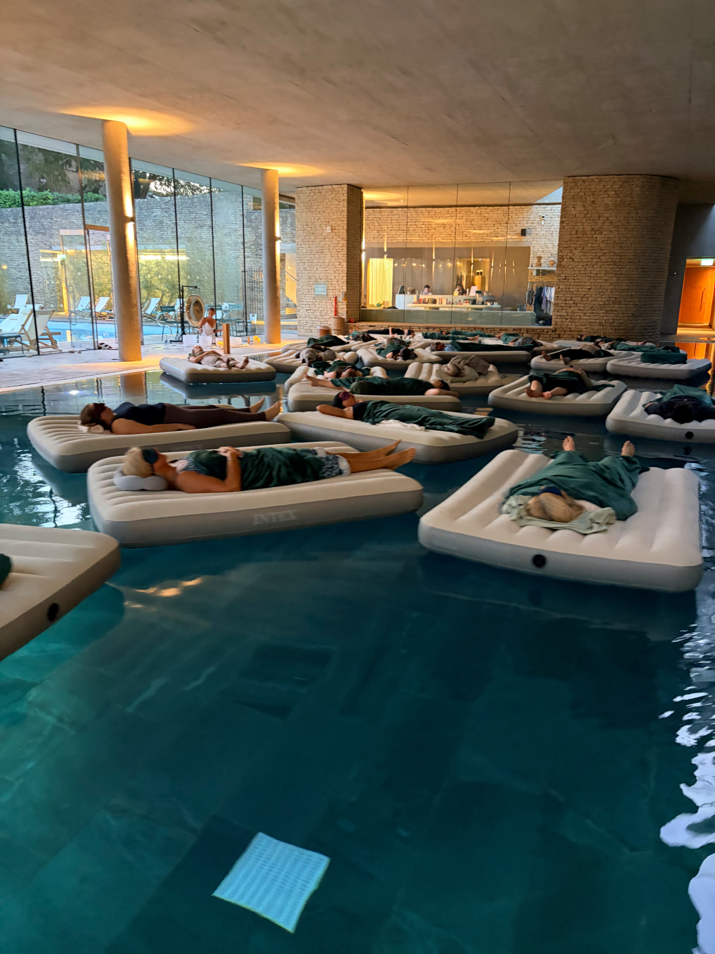 Guests resting on floating beds across the indoor pool at a Floating Sound Sanctuary session at Cowley Manor