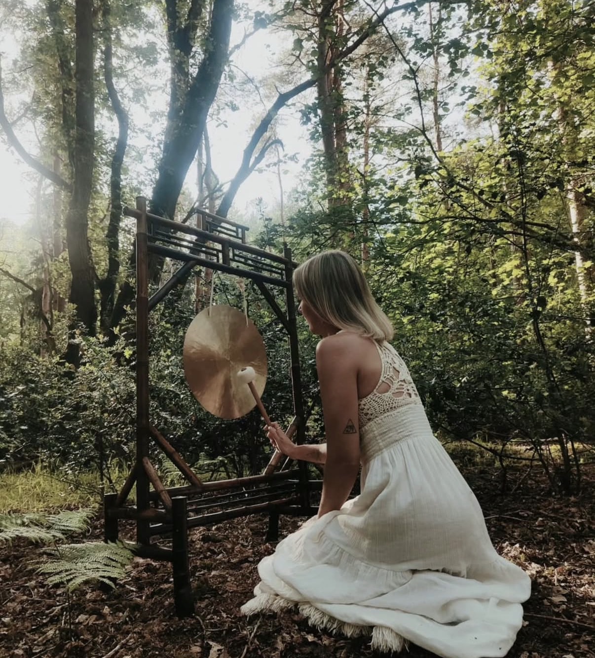 April playing a gong in a sunlit woodland setting